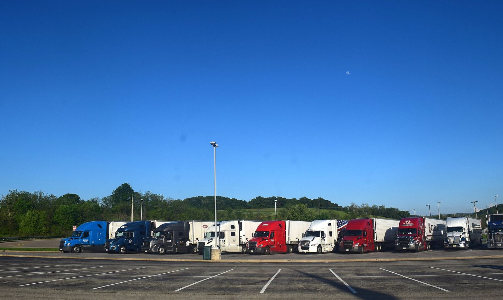 Tractors parked in a line at a truck stop under a clear sky.